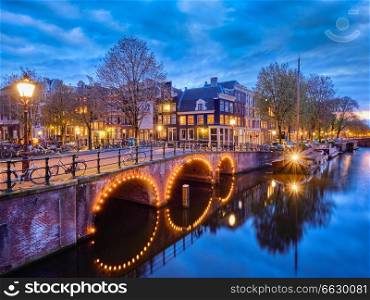Night view of Amterdam cityscape with canal, bridge and medieval houses in the evening twilight illuminated. Amsterdam,  Netherlands. Amterdam canal, bridge and medieval houses in the evening