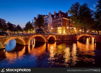 Night view of Amterdam cityscape with canal, bridge and medieval houses in the evening twilight illuminated. Amsterdam, Netherlands. Amterdam canal, bridge and medieval houses in the evening
