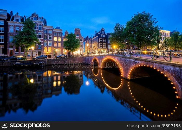 Night view of Amterdam cityscape with canal, bridge and medieval houses in the evening twilight illuminated. Amsterdam, Netherlands. Amterdam canal, bridge and medieval houses in the evening