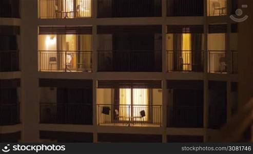 Night view of hotel building. Light in several apartments, chairs and tables on the balconies
