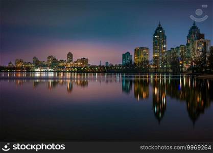 Night view of modern buildings in the Obolon district of Kiev, Ukraine, close to the Dnieper River, The lights reflect on the calm water.