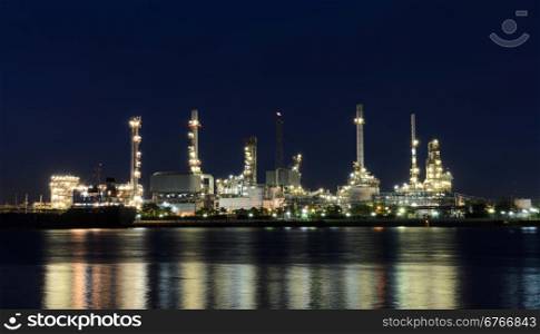 Night view of oil refinery plant illuminated at night with reflection on the river