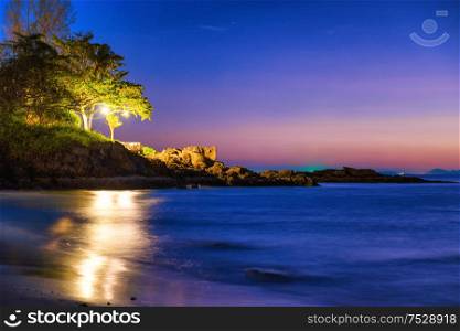 Night view of sand beach, sea and rocky shore with trees at tropical island