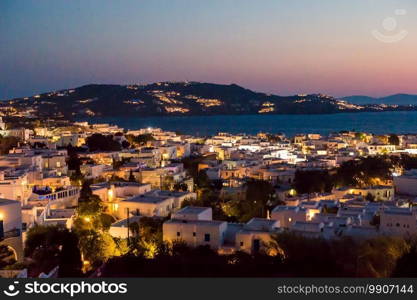 Night village in the lights against the backdrop of the sea at sunset. Beautiful colorful sunset of amazing greek town Mykonos
