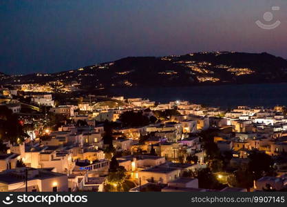 Night village in the lights against the backdrop of the sea at sunset. Beautiful colorful sunset of amazing greek town Mykonos