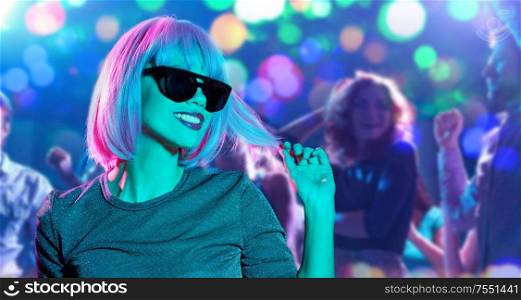 nightlife and entertainment concept - happy young woman wearing pink wig and black sunglasses in neon ultra violet light over people dancing at nightclub background. happy woman in pink wig and black sunglasses