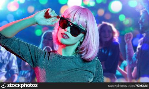 nightlife, entertainment and people concept - happy young woman in pink wig and black sunglasses at nightclub over lights background. woman in pink wig and sunglasses at nightclub