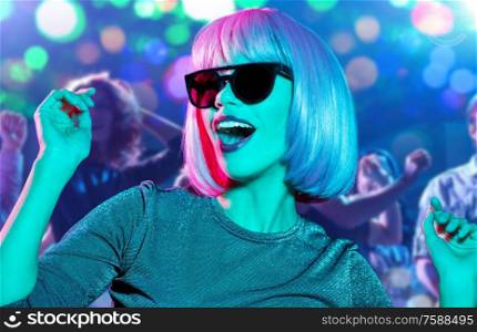 nightlife, entertainment and people concept - happy young woman wearing pink wig and black sunglasses dancing at nightclub over lights background. woman in wig and sunglasses dancing at nightclub