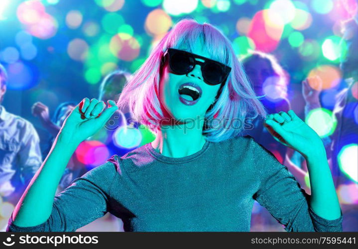 nightlife, entertainment and people concept - happy young woman wearing pink wig and black sunglasses dancing at nightclub over lights background. woman in wig and sunglasses dancing at nightclub