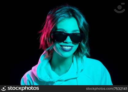 nightlife, fashion and people concept - happy young woman wearing hoodie in neon lights over black background. woman wearing hoodie in neon lights over black