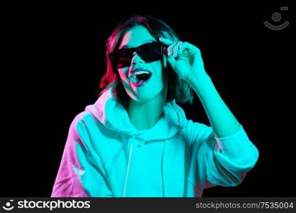 nightlife, fashion and people concept - happy young woman wearing hoodie in neon lights over black background. woman wearing hoodie in neon lights over black