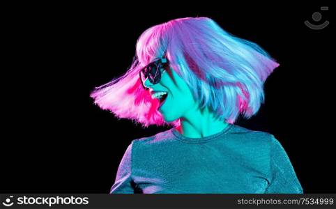 nightlife, fashion and people concept - happy young woman wearing pink wig and black sunglasses in neon ultra violet light dancing over black background. happy woman in pink wig and sunglasses dancing