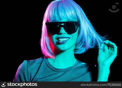 nightlife, fashion and people concept - happy young woman wearing pink wig and black sunglasses in neon ultra violet light over black background. happy woman in pink wig and black sunglasses