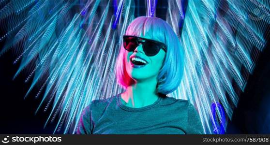 nightlife, fashion and people concept - happy young woman wearing pink wig and black sunglasses in neon ultra violet light over neon lights on black background. happy woman in pink wig and black sunglasses