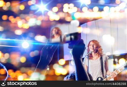 nightlife, music, technology and people concept - close up of singer playing electric guitar and singing on stage over fans crowd taking picture or video by tablet pc computer at concert in night club