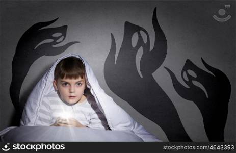 Nightmares of child. Little scared boy in bed under blanket with flashlight