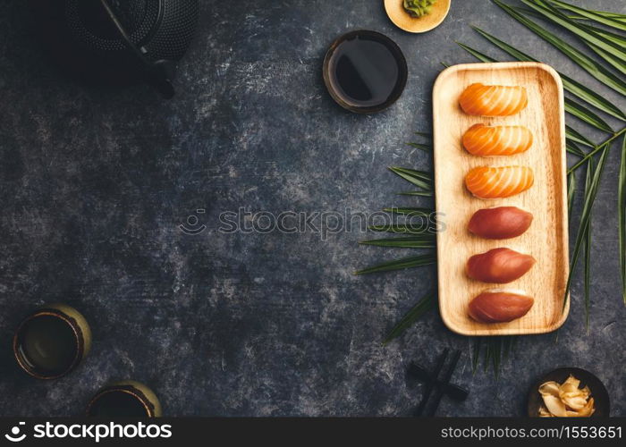 Nigiri sushi set with salmon and tuna served on bamboo plate with chopsticks, soy sause, wasabi, ginger and tea on dark background. Delicious traditional Japanese food, top view, flat lay, copy space