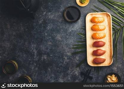 Nigiri sushi set with salmon and tuna served on bamboo plate with chopsticks, soy sause, wasabi, ginger and tea on dark background. Delicious traditional Japanese food, top view, flat lay, copy space
