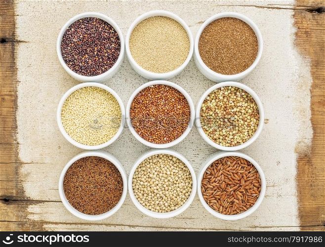 nine healthy, gluten free grains (quinoa, brown rice, millet, amaranth, teff, buckwheat, sorghum), kaniwa), top view of small round bowls against rustic barn wood