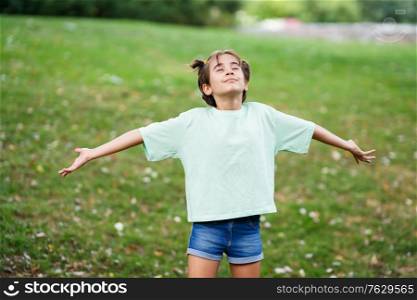 Nine-year-old girl breathing with open arms on the grass of an urban park.. Nine-year-old girl breathing with open arms on the grass