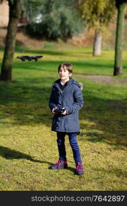 Nine-year-old girl operating toy drone flying or hovering by remote control in a park.. Nine-year-old girl operating toy drone flying by remote control