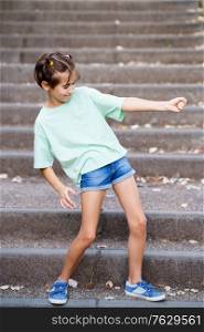 Nine-year-old girl playing air guitar on the steps of a city park.. Nine-year-old girl playing air guitar in an urban park
