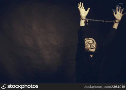 No freedom, social problems concept. Furious man with chained hands, studio shot on dark grunge background. Furious man with chained hands, no freedom