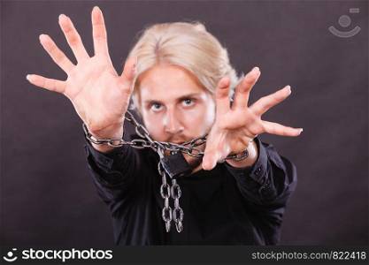 No freedom, social problems concept. Furious man with chained hands, studio shot on dark grunge background. Scared man with chained hands, no freedom