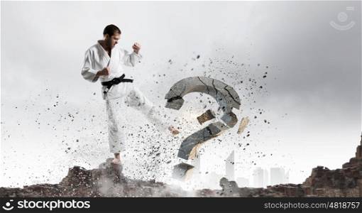 No more doubts. Young determined karate man breaking with leg concrete question sign