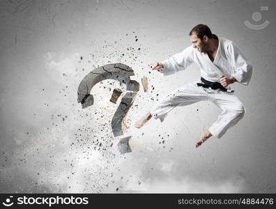 No more doubts. Young determined karate man breaking with leg concrete question sign