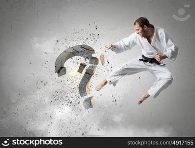 No more doubts. Young determined karate man breaking with leg concrete question sign