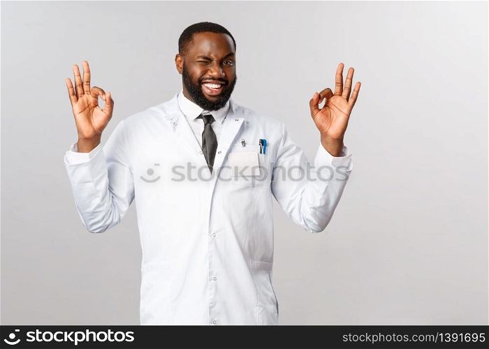No problem, clinic guarantee best professional service and caring. African-american easy-going male doctor in white coat, wink cheeky and show okay signs as recommend or assure you be fine.. No problem, clinic guarantee best professional service and caring. African-american easy-going male doctor in white coat, wink cheeky and show okay signs as recommend or assure you be fine