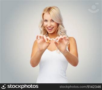 no smoking, addiction and people concept - happy young woman breaking cigarette over gray background. happy young woman breaking cigarette over gray