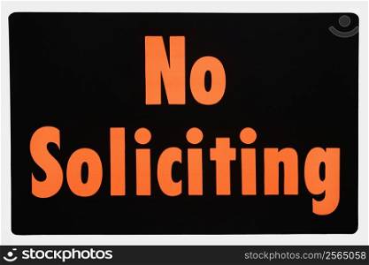 No soliciting sign with orange text against black.