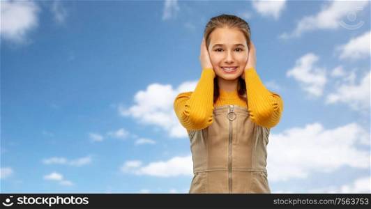 noise, hearing and people concept - smiling teenage girl closing ears by hands over blue sky and clouds background. smiling teenage girl closing ears over sky