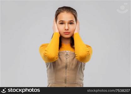 noise, hearing and people concept - smiling teenage girl closing ears by hands over grey background. smiling teenage girl closing ears by hands