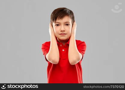 noise, silence and people concept - portrait of little boy in red polo t-shirt closing ears by hands over grey background. boy in red t-shirt closing ears by hands