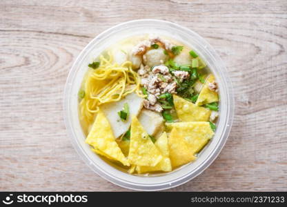 noodles pork balls fish balls and minced pork with crispy wontons and vegetable in plastic bowl on wooden table, top view Thai and China Asian food delivery concept