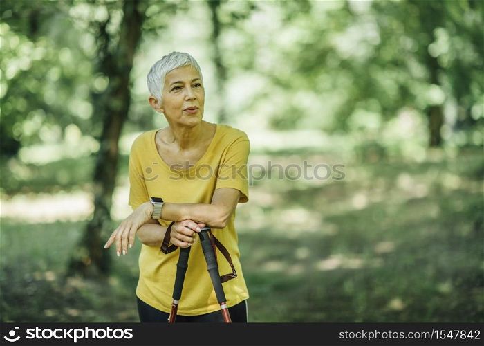 Nordic walking - active senior woman taking a break, enjoying the nature. Nordic Walking - Active Senior Woman Taking a Break