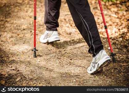 Nordic walking. Closeup of female legs hiking in the forest or park. Active and healthy lifestyle.