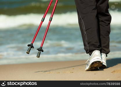 Nordic walking. Closeup of female legs hiking on the beach. Active and healthy lifestyle.