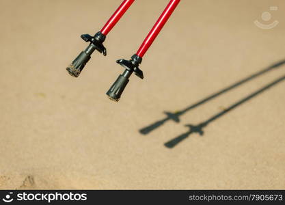 Nordic walking equipment. Closeup of red sticks on the sandy beach. Active and healthy lifestyle.