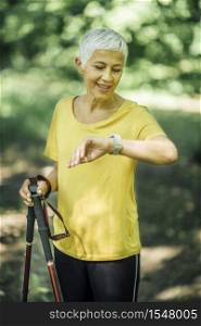 Nordic walking exercise. mature woman checking heart rate tracker during exercise break . Nordic Walking Exercise
