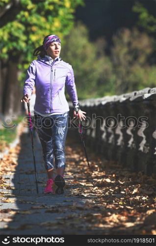 Nordic walking on sidewalk. A young woman practices it and relaxes after a day at work
