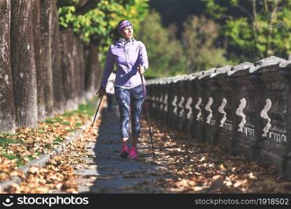 Nordic walking on sidewalk. A young woman practices it and relaxes after a day at work