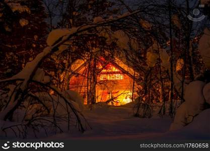 Northern Finland. Thick winter forest and a lot of snow. Small wooden house and night lighting. Lighted Wooden House in the Night Winter Forest