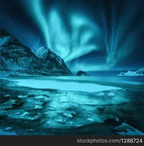 Northern lights and snowy mountains, frozen sea coast and reflection in water in Lofoten islands, Norway. Aurora borealis. Winter landscape with polar lights, ice in water. Starry sky with aurora