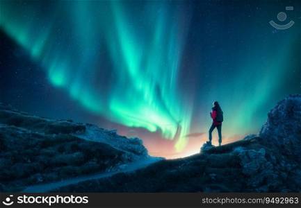 Northern lights and woman on mountain peak at night. Aurora borealis and silhouette of alone girl on mountain trail. Landscape with polar lights. Sky with stars and bright aurora. Travel background