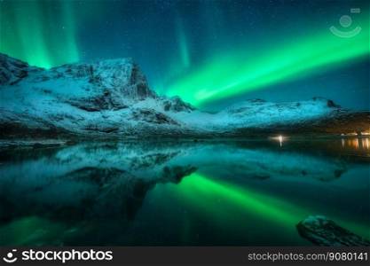 Northern lights over the snowy mountains, sea, reflection in water at night in Lofoten, Norway. Aurora borealis and snow covered rocks. Winter landscape with polar lights, sky with stars and fjord