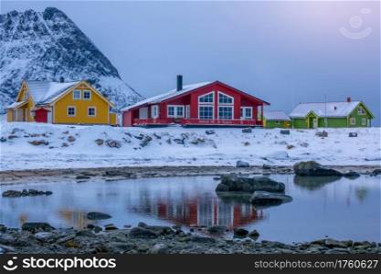 Norway. Multi-colored cottages on the background of the mountains on the shore of the fjord. Winter evening. Low Tide in the Fjord and Norwegian Cottages in the Winter Evening